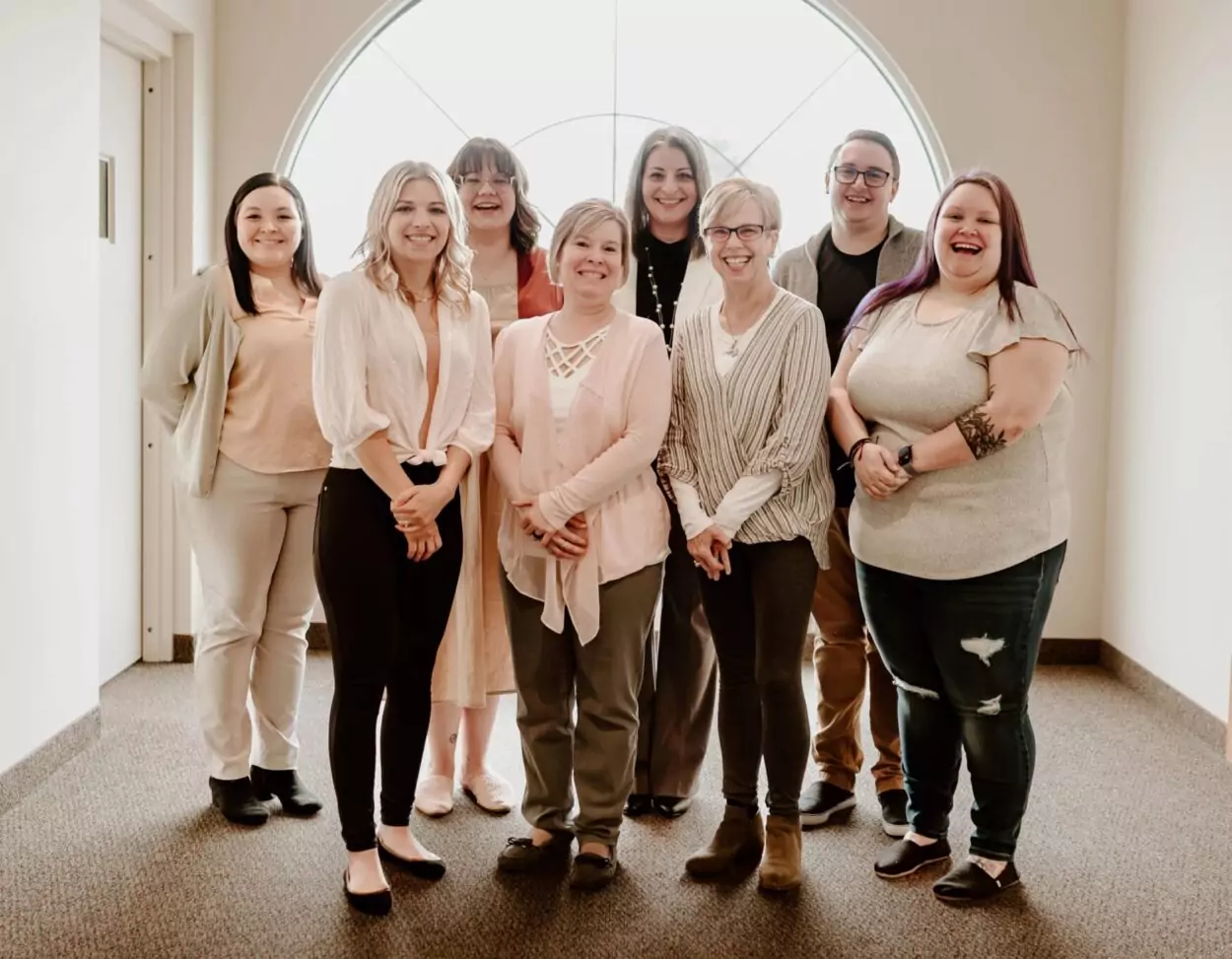 Group shot of the staff of Intera standing in front of a bay window. Back row from left to right: Alexis, Amanda, Mary, and Jarrod. Front row from left to right: Rosemary, Angela, Sandy, and Taylour.