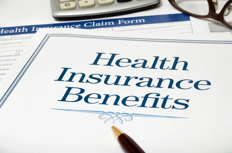 Health Insurance Benefits paperwork, pen, glasses, and calculator.