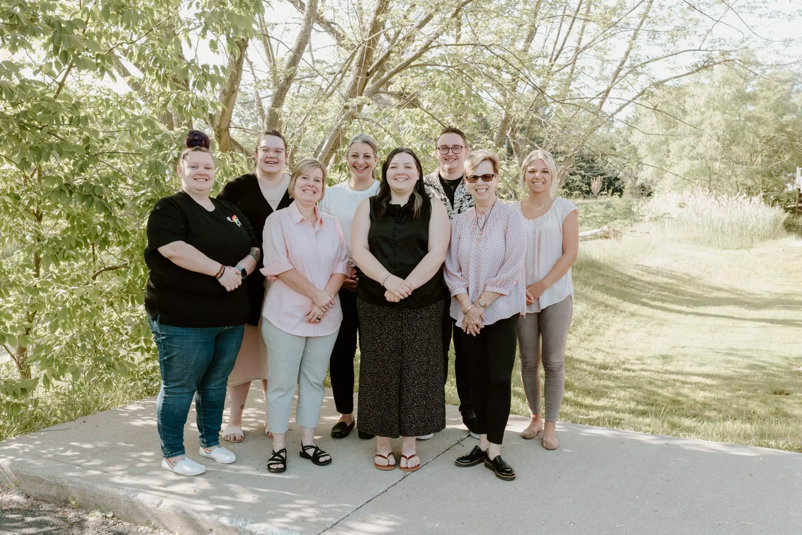 Group photo of the Intera staff outside, on a sidewalk, in front of green trees and grass. Front row L-R; Taylour, Angela, Alexis, and Sandy. Back row L-R; Amanda, Mary, Jared, and Rosemary.