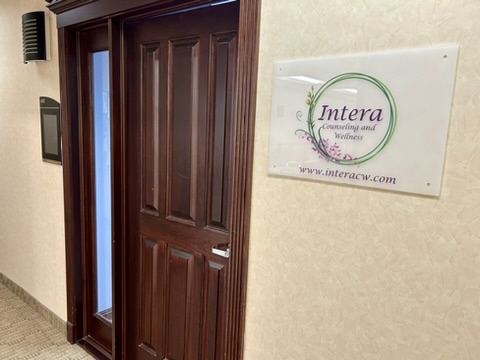View of a dark wood door in a hallway with the Intera sign on the wall to the right of the door.